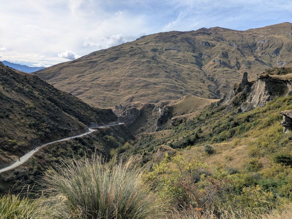 A gravel switchback road winding through tussock-covered hills in New Zealand's South Island