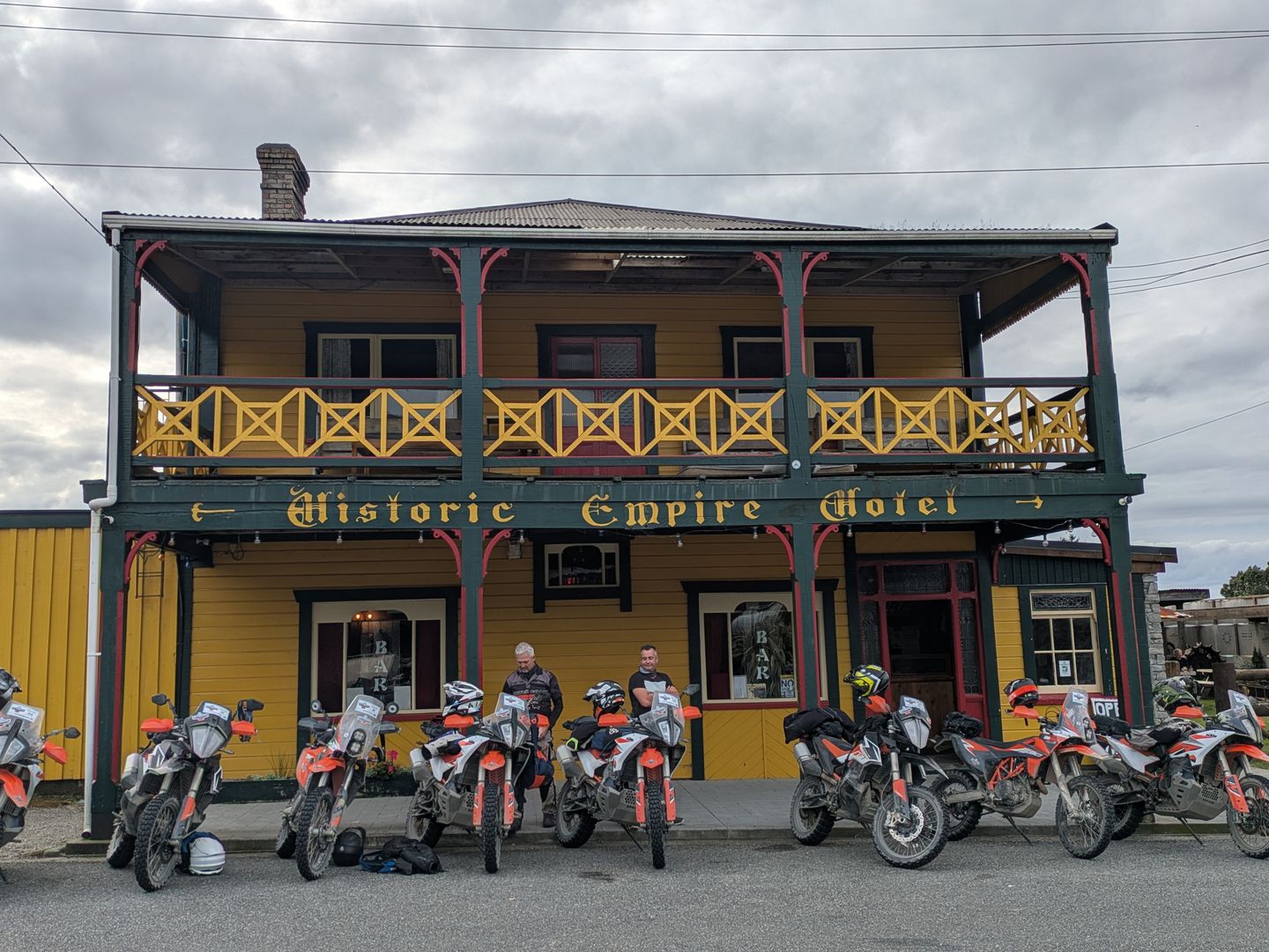 A two-story yellow 19th-century hotel facade with a wraparound balcony, several KTM motorcycles parked in front